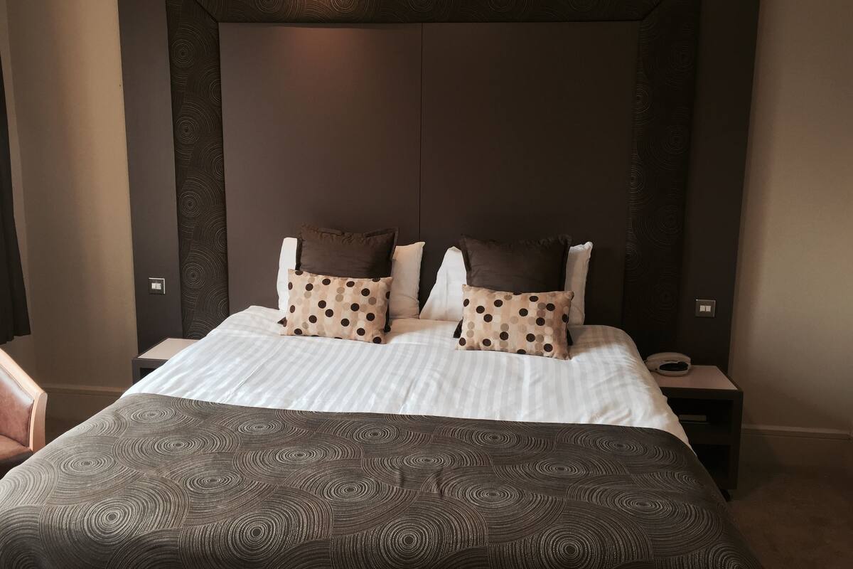 Een netjes opgemaakt bed met een bedovertrek met patroon en twee kussens met stippen.