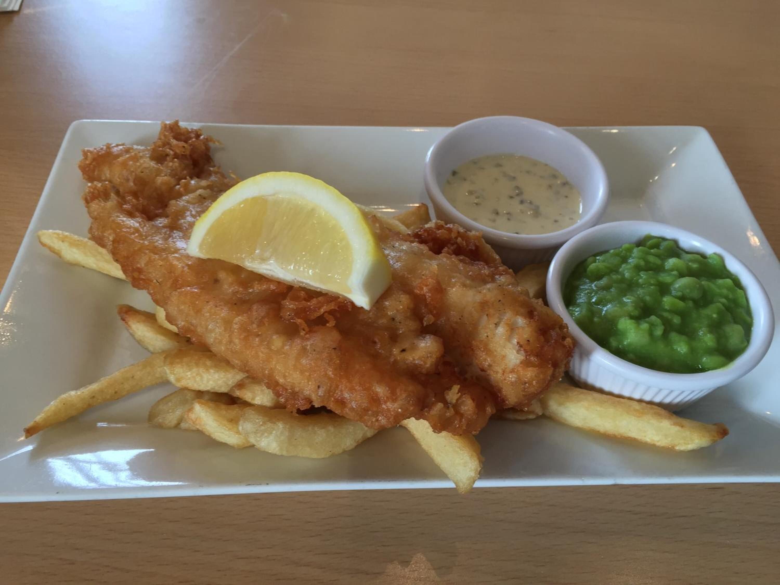 A plate of fish and chips with lemon wedge, tartar sauce, and mushy peas.