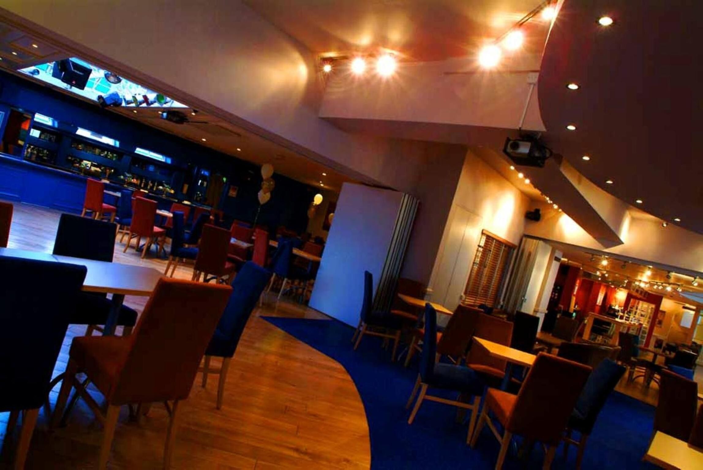 A modern bar area with a curved seating arrangement, a bar counter, and a television screen displaying a sports event.