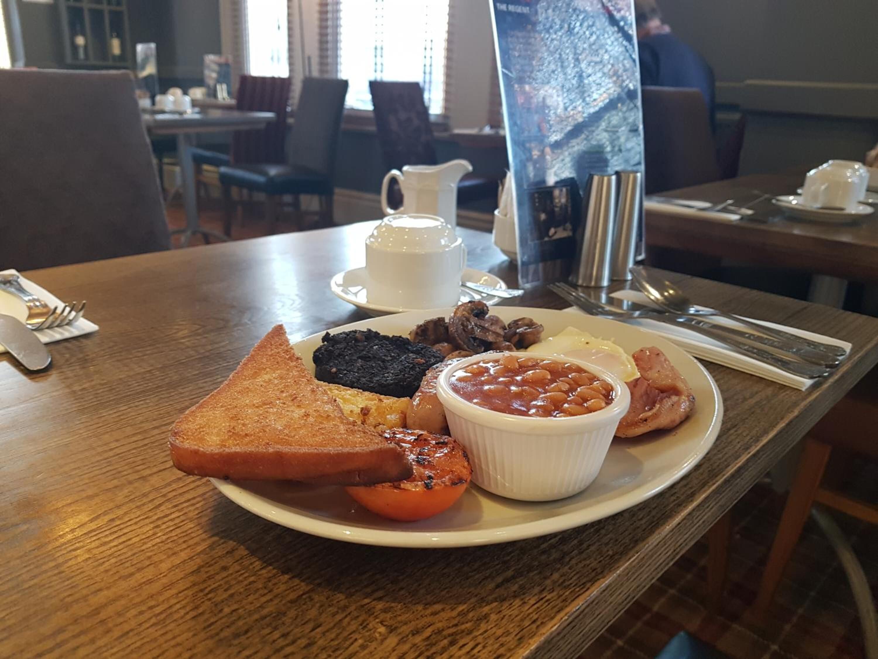 Un plato de desayuno con tostadas, frijoles, huevos y tomates sobre una mesa de madera en un restaurante.
