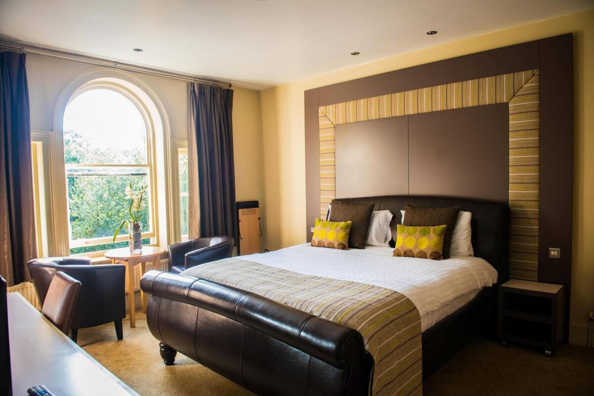 Een hotelkamer met een groot bed, een bureau, een stoel en uitzicht op groen buiten het raam.