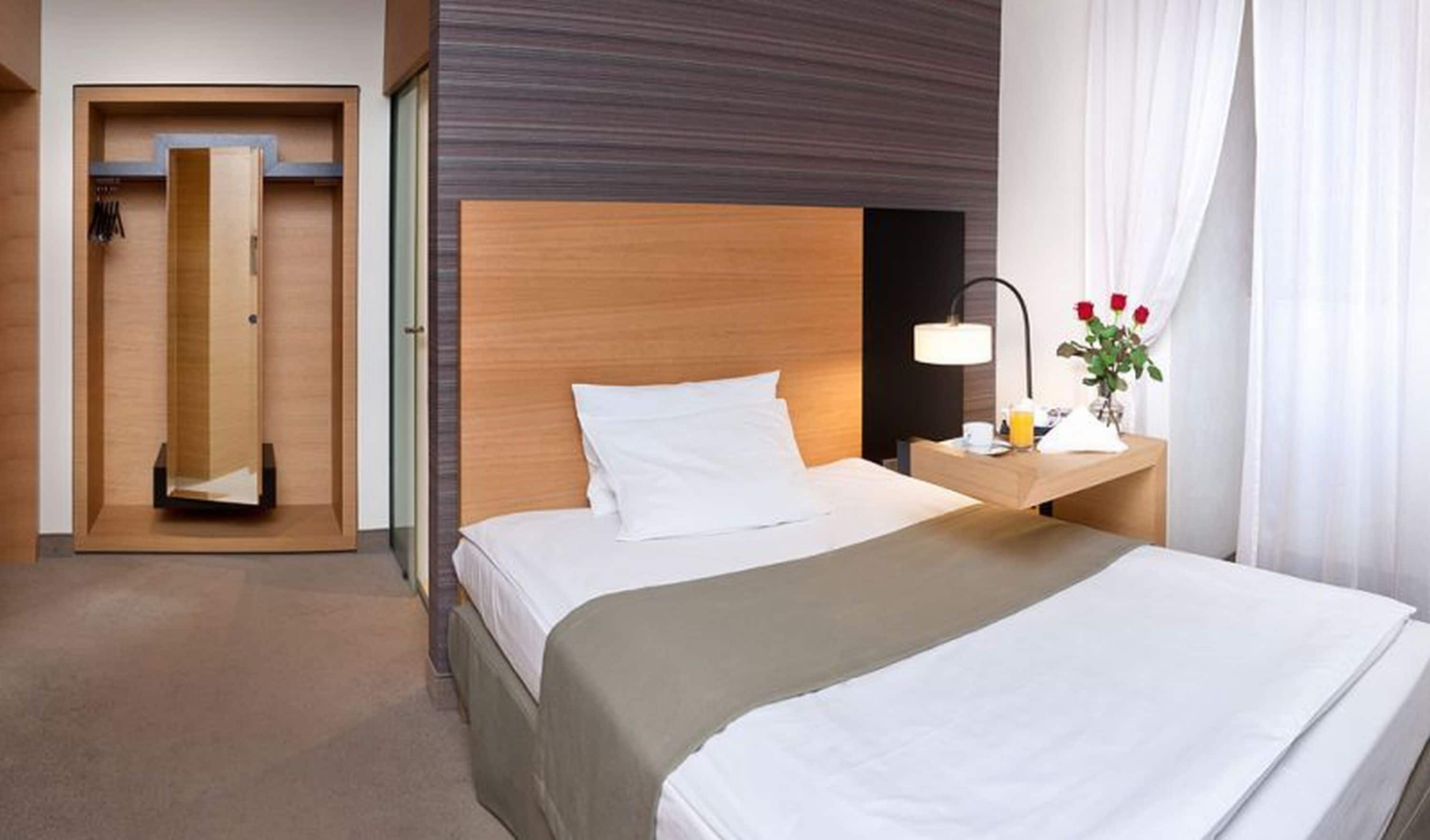 A hotel room with a bed, bedside table, lamp, and a small table with a vase of flowers.