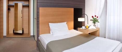 Habitación de hotel con cama, mesita de noche, lámpara y una pequeña mesa con un florero.