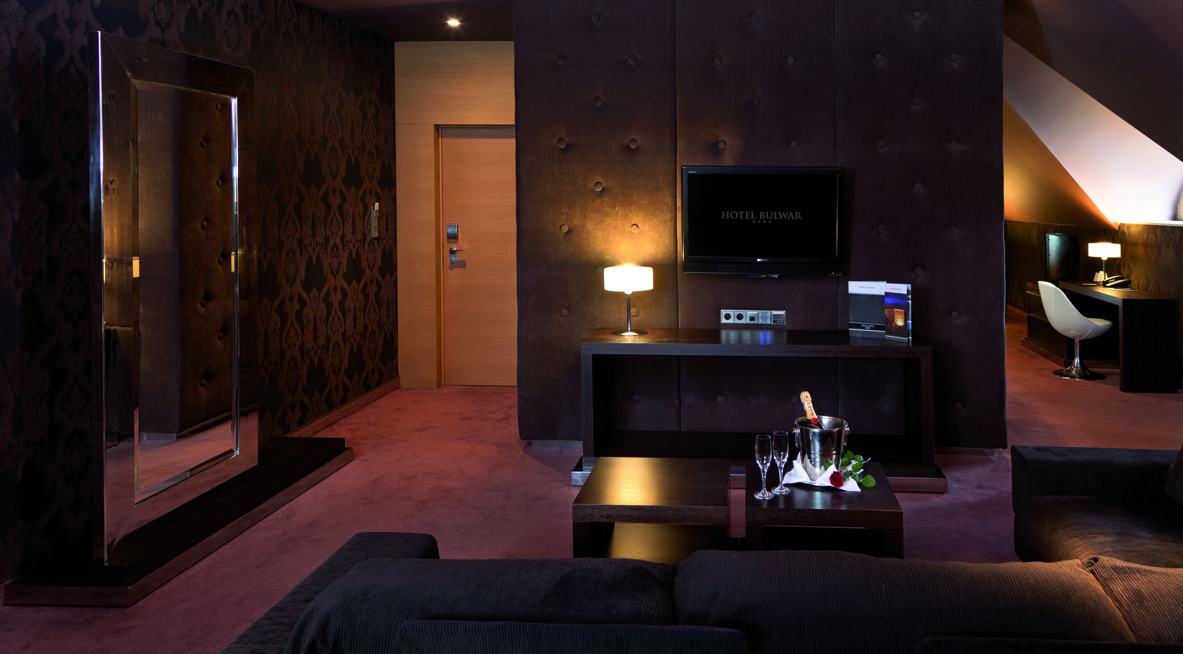 Un hall d’hôtel moderne avec un canapé, un téléviseur, un bureau avec une lampe et un comptoir d’accueil.