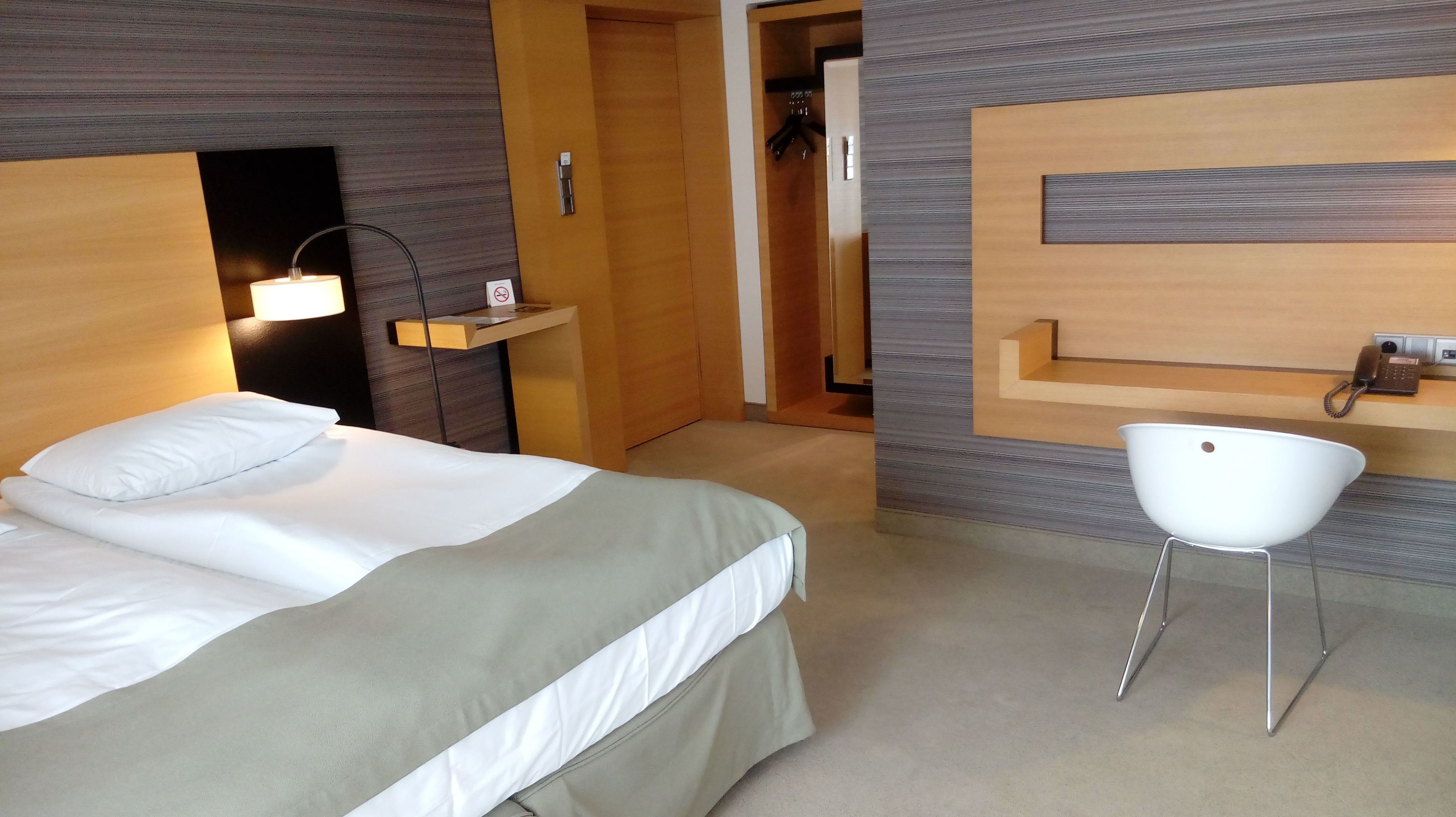 Et hotelværelse med en seng, et natbord med lampe, en stol og et skrivebord med telefon.