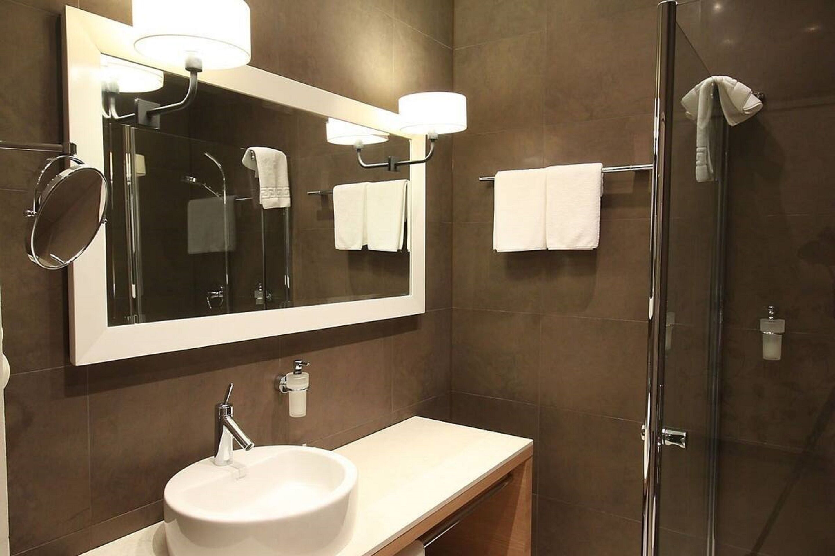 A modern bathroom with a large mirror, a white sink, and a glass-enclosed shower.