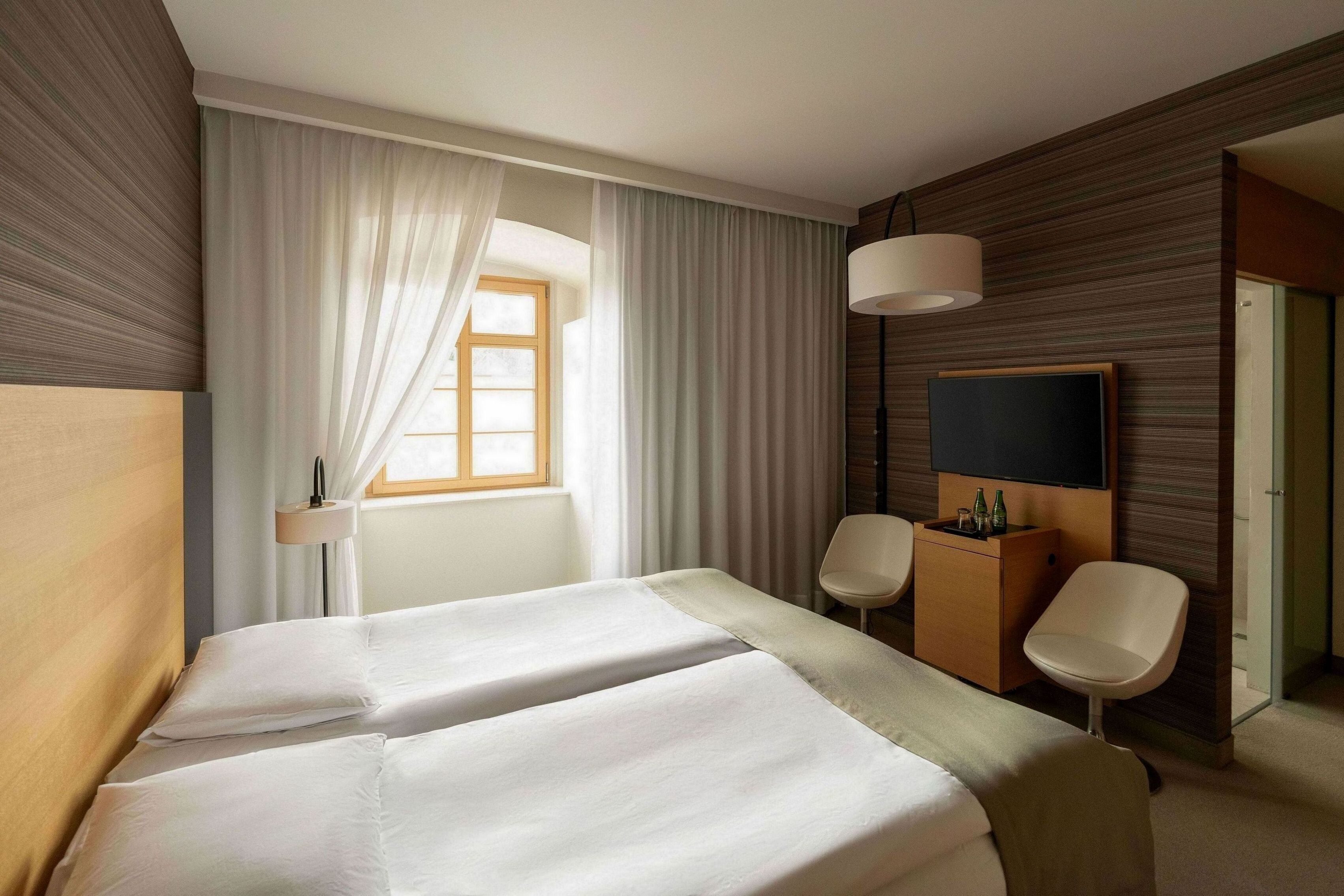 Una camera d'albergo con due letti, una TV, una scrivania con una lampada e una sedia.