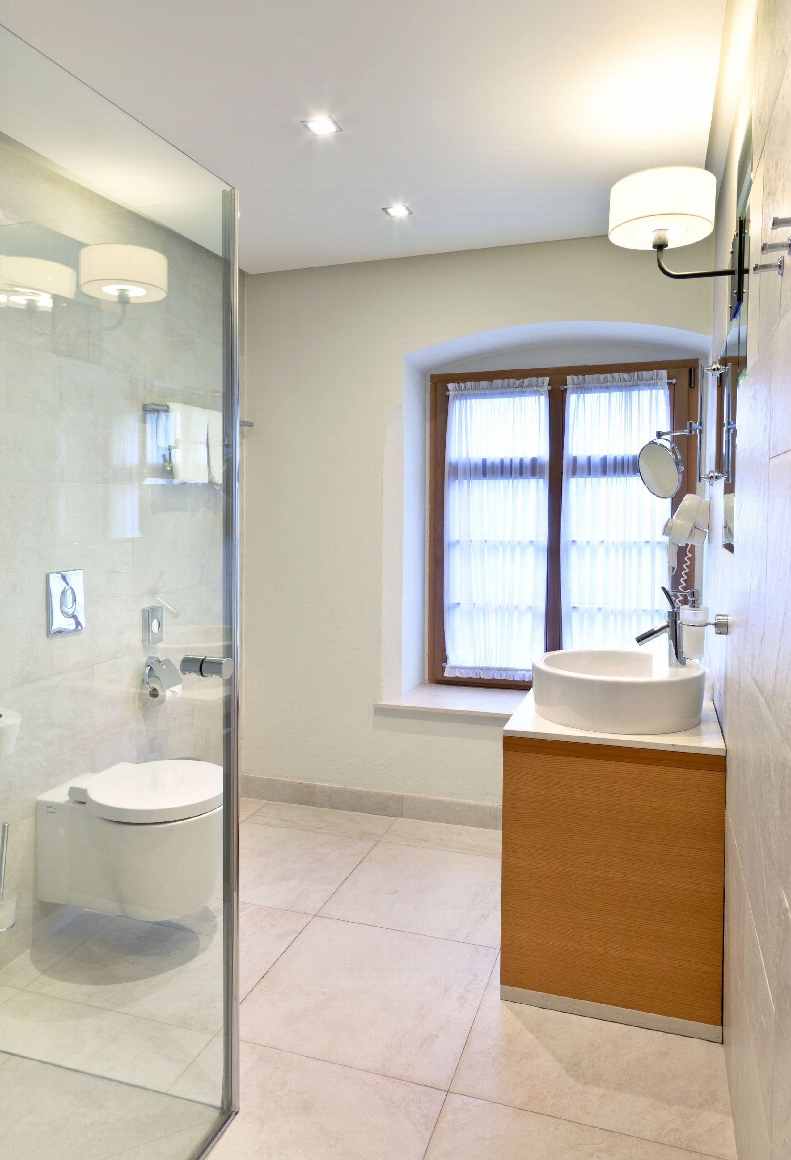 A modern bathroom with a glass-enclosed shower, a white sink, and a window with curtains.