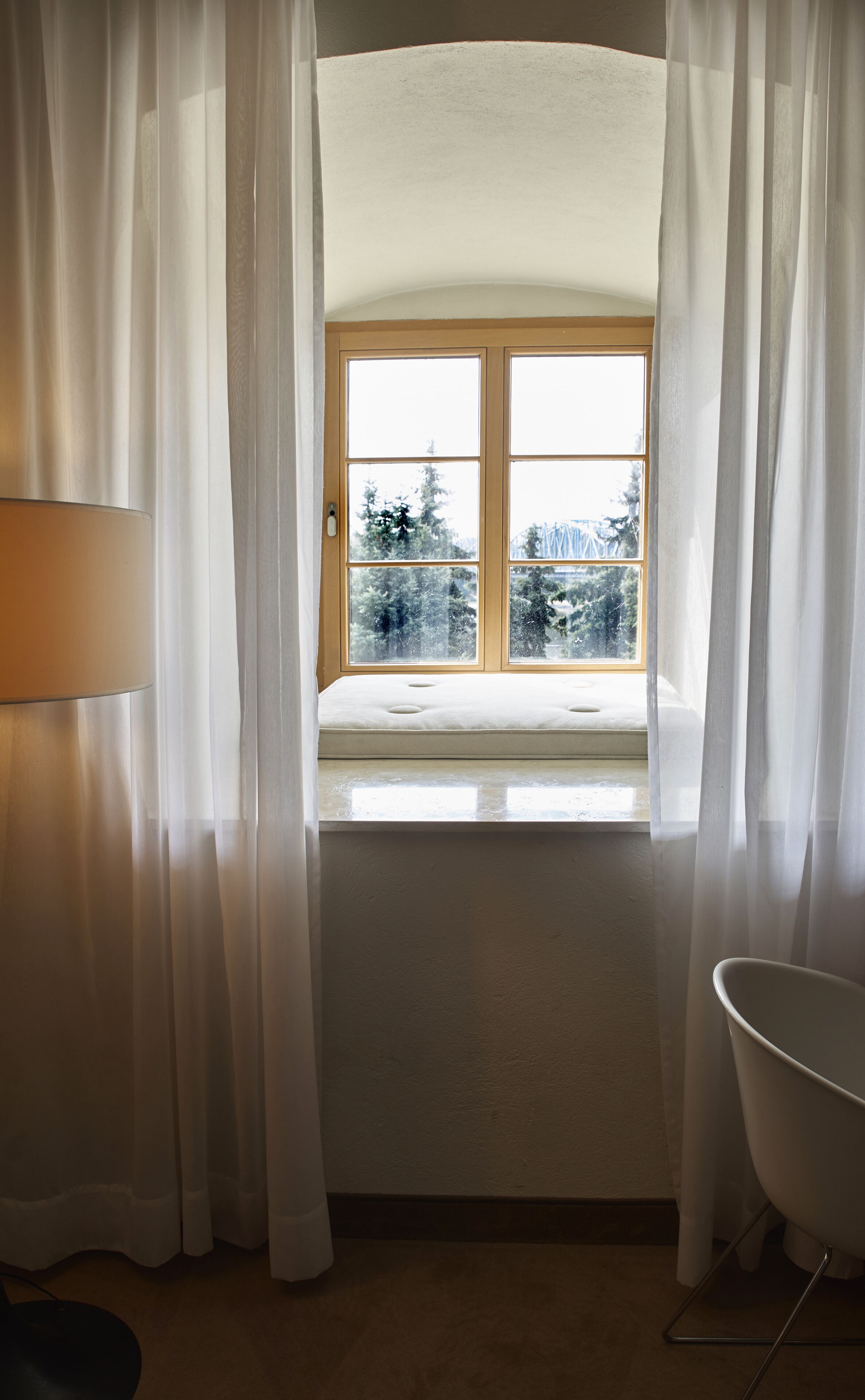 A room with a window, curtains, a chair, and a lamp.