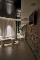 Un pasillo moderno de hotel con pared de ladrillo, un sofá con cojines y un televisor montado en la pared.