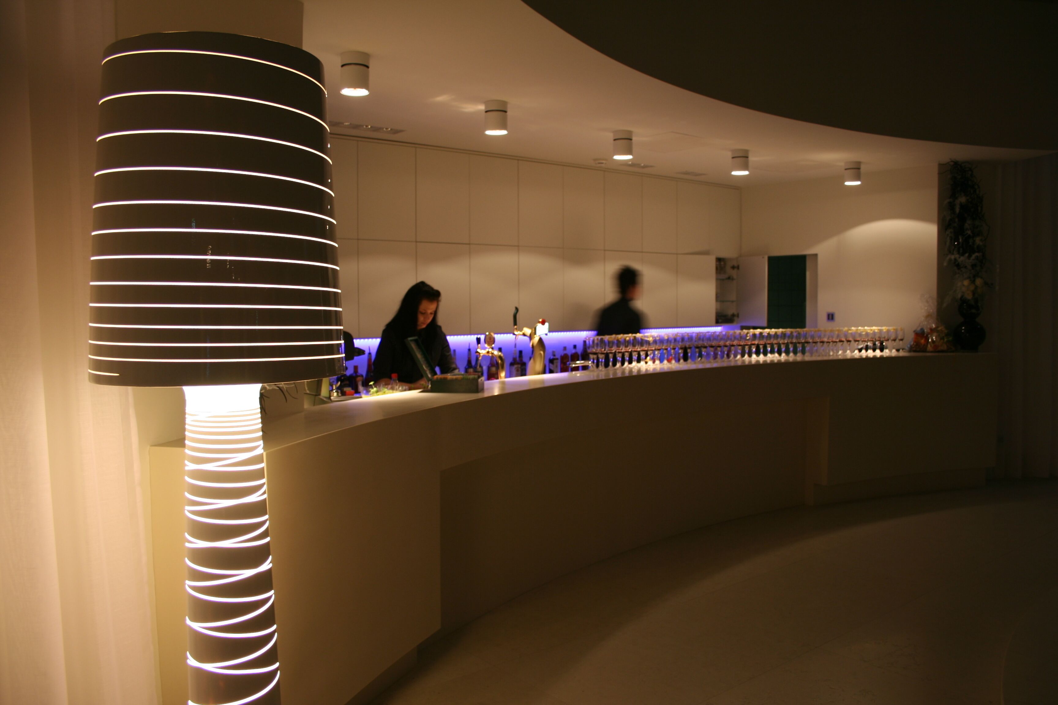 A modern bar area with a curved counter, ambient lighting, and a decorative column.