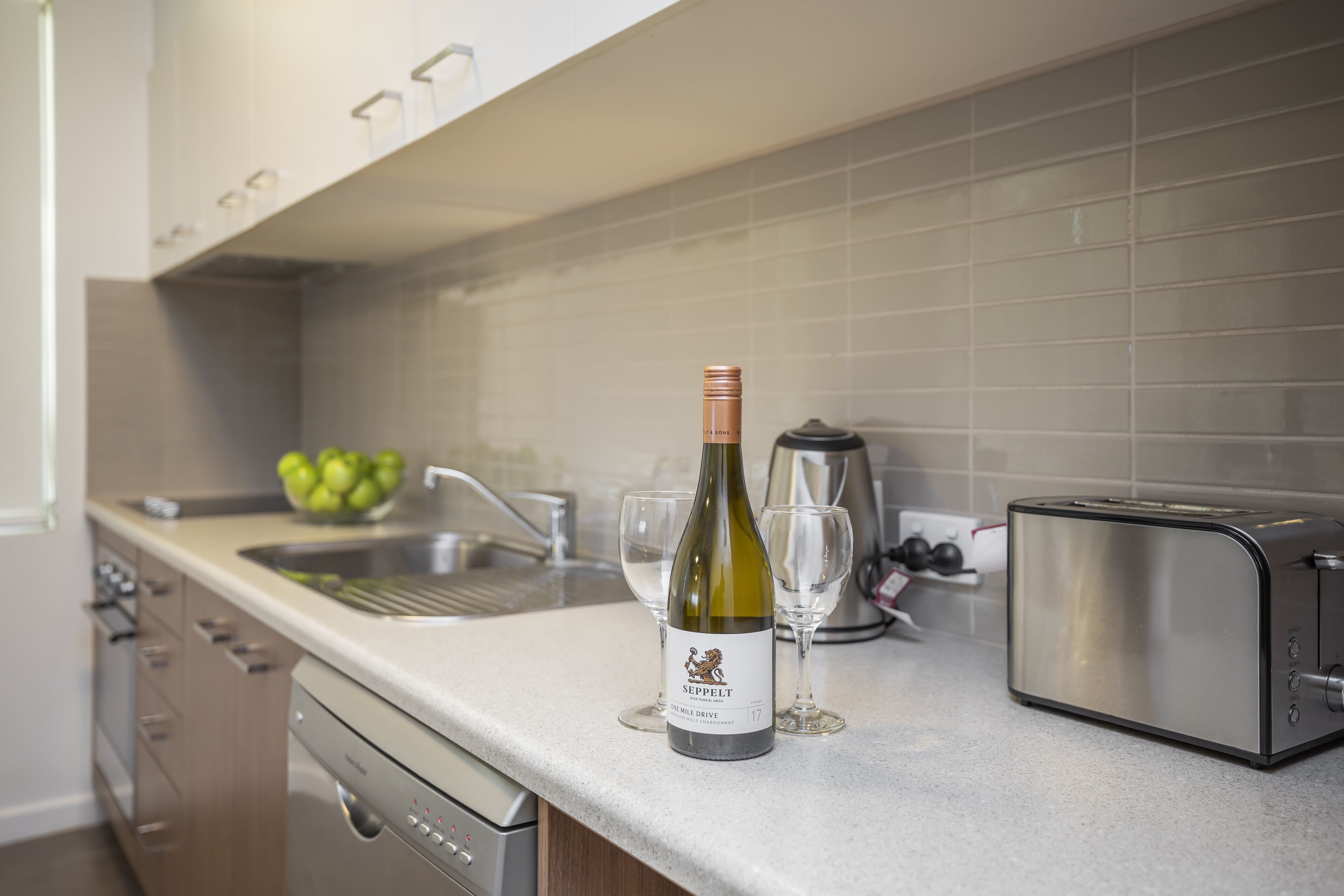 A kitchen with a wine bottle, a toaster, and a sink.