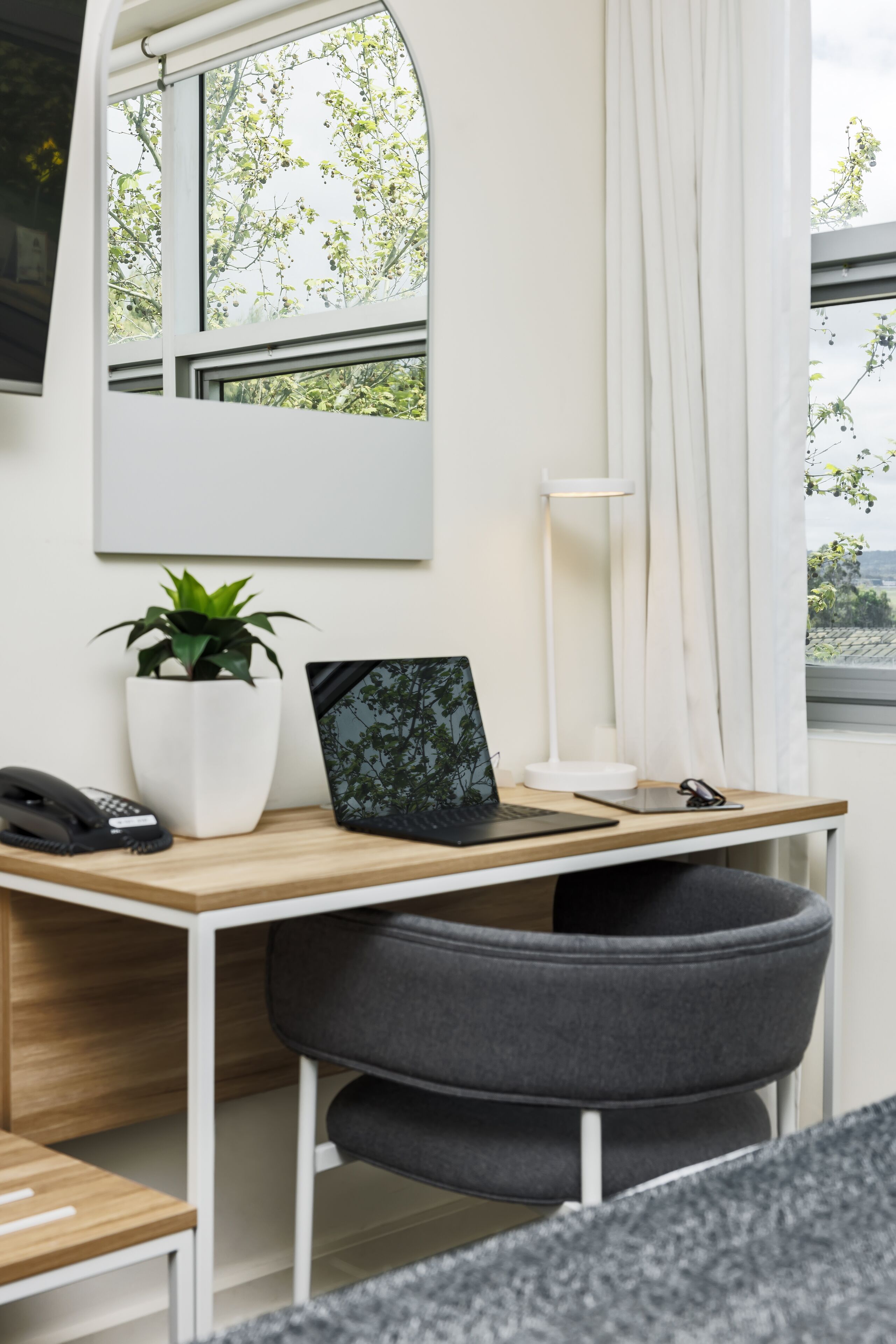 A modern workspace with a desk, chair, laptop, potted plant, and a lamp.