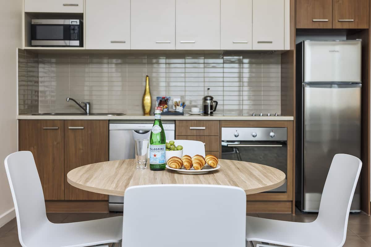Une cuisine moderne avec des meubles blancs, un réfrigérateur en acier inoxydable, un four à micro-ondes et une table à manger en bois, assortie de chaises blanches.
