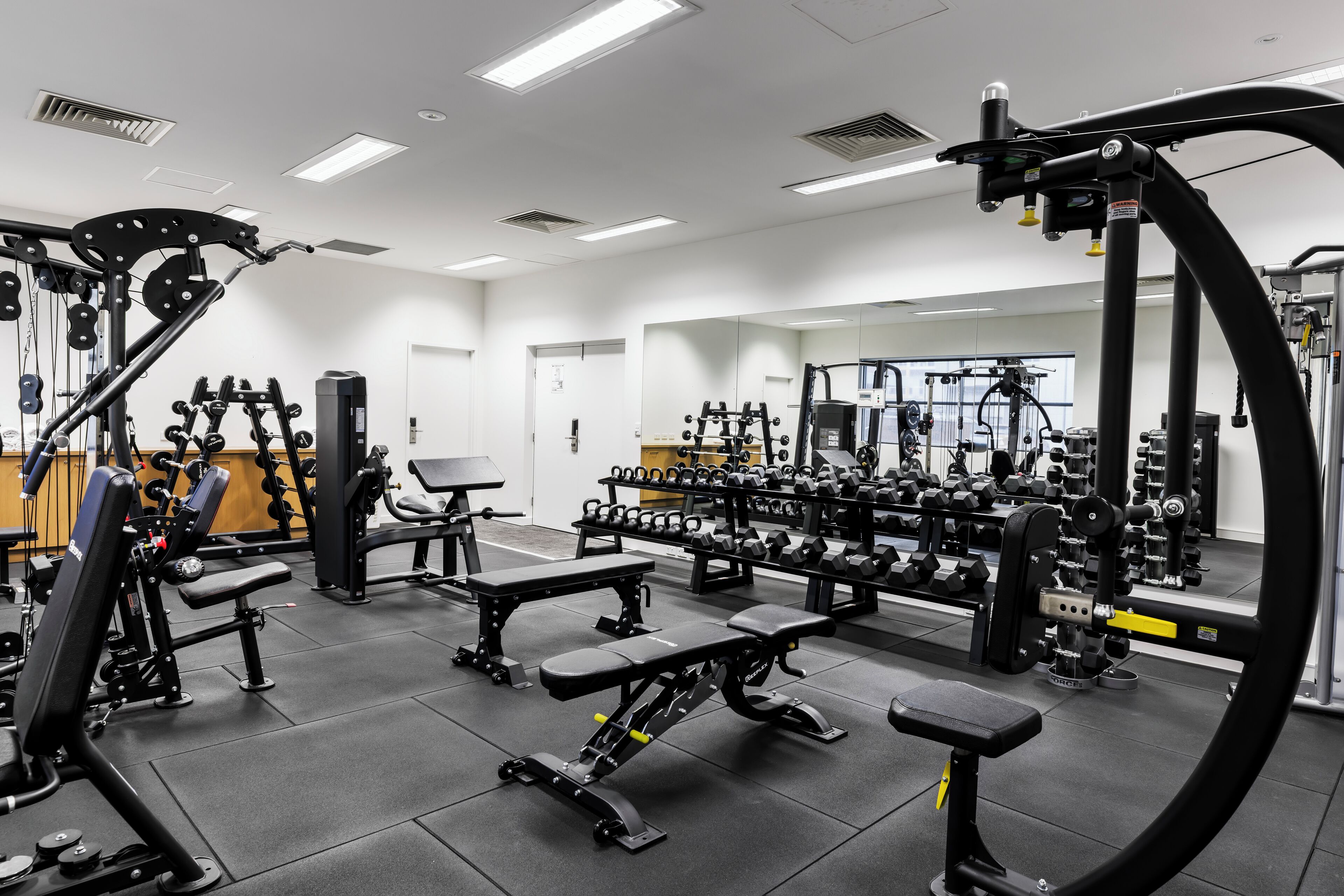 Ein Fitnessstudio mit verschiedenen Trainingsgeräten, Bänken und Gewichtsständern.