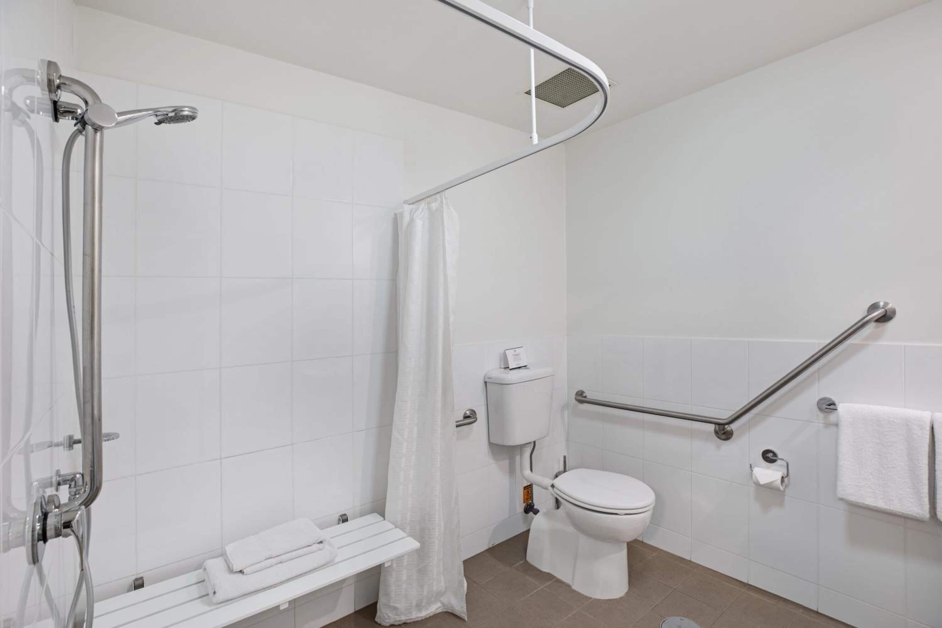 A modern bathroom with a shower, toilet, and grab bars.