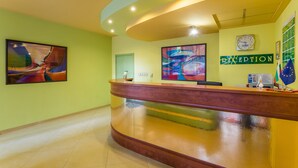A reception area with a curved wooden reception desk, a clock, and two large abstract paintings on the walls.