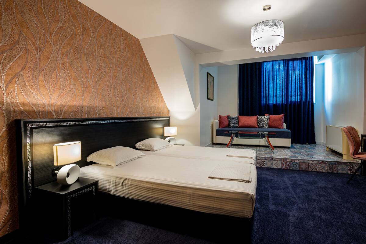 A hotel room with a bed, nightstands, a sofa, and a chandelier.
