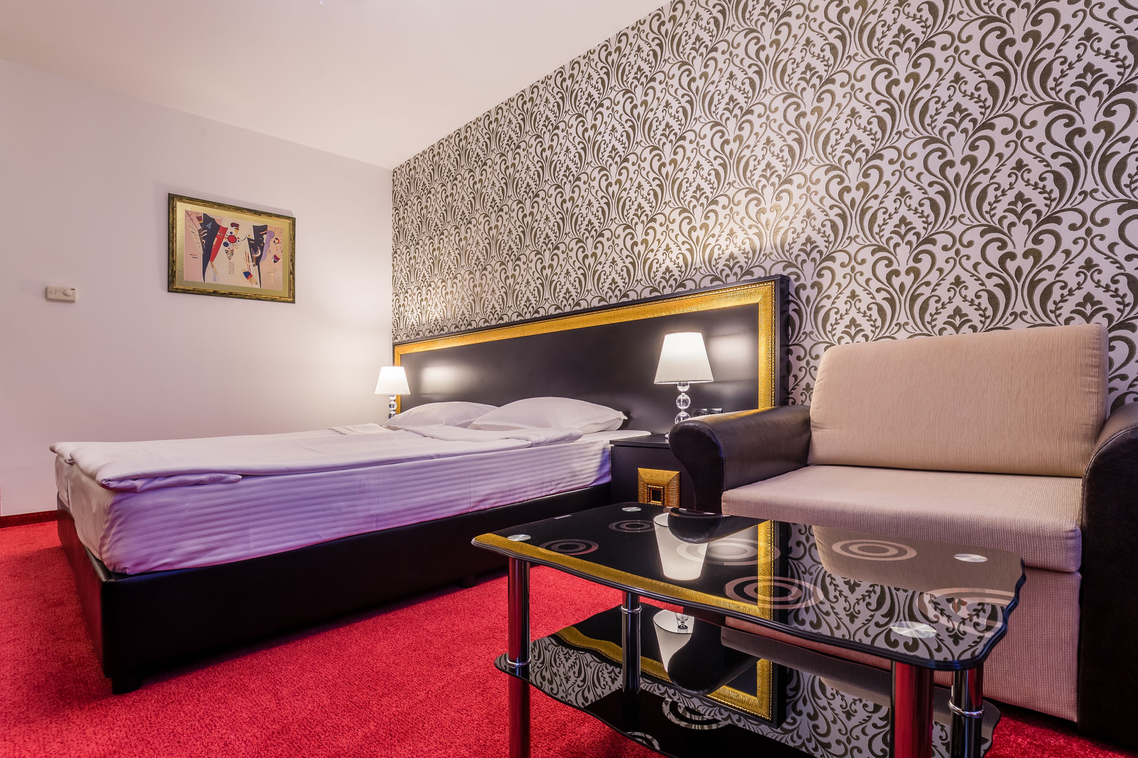 Une chambre d’hôtel avec un lit, un canapé, une petite table et un papier peint à motifs.