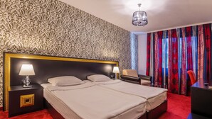 A hotel room with a large bed, two bedside tables with lamps, a desk, and a chair.