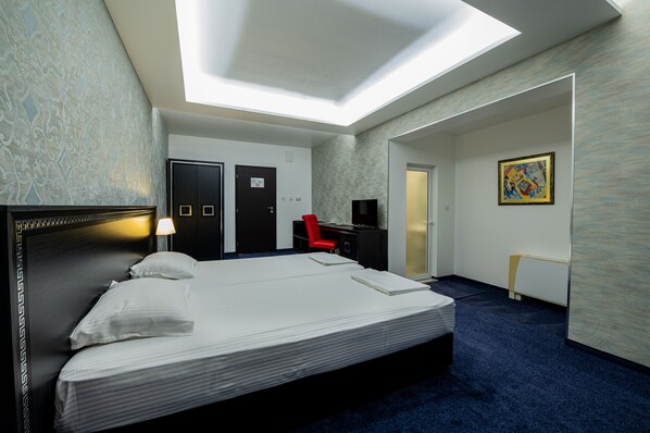 Una habitación de hotel con una cama grande, un escritorio, una silla, un televisor y una mesita.