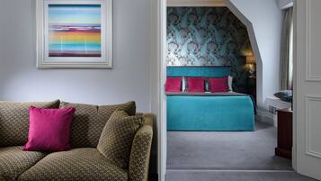 A room with a patterned sofa, a framed painting, and a bed with teal bedding and patterned wallpaper.