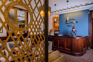 A reception area with a receptionist, a blue wall with the hotel name, and a decorative golden partition.