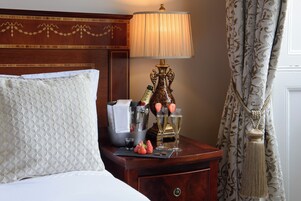 A hotel room with a bed, a nightstand with a lamp, a bottle of champagne, and strawberries.