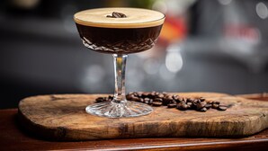 A cocktail in a glass on a wooden board with coffee beans around it.