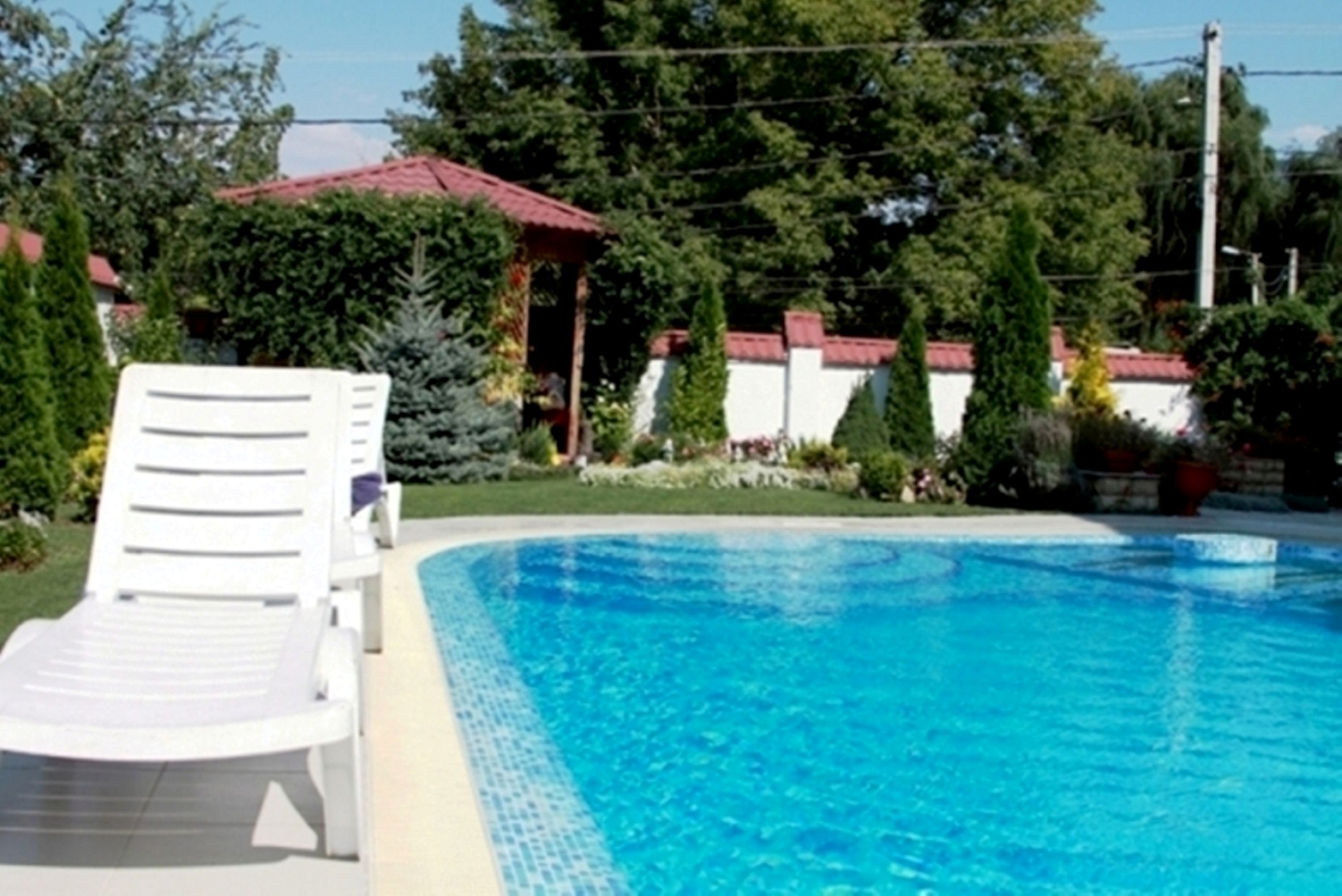 Uma piscina com uma espreguiçadeira branca, rodeada por vegetação e uma estrutura com telhado vermelho.