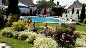 A swimming pool surrounded by lush greenery and white flowers. - Edem Hotel (Chisinau)