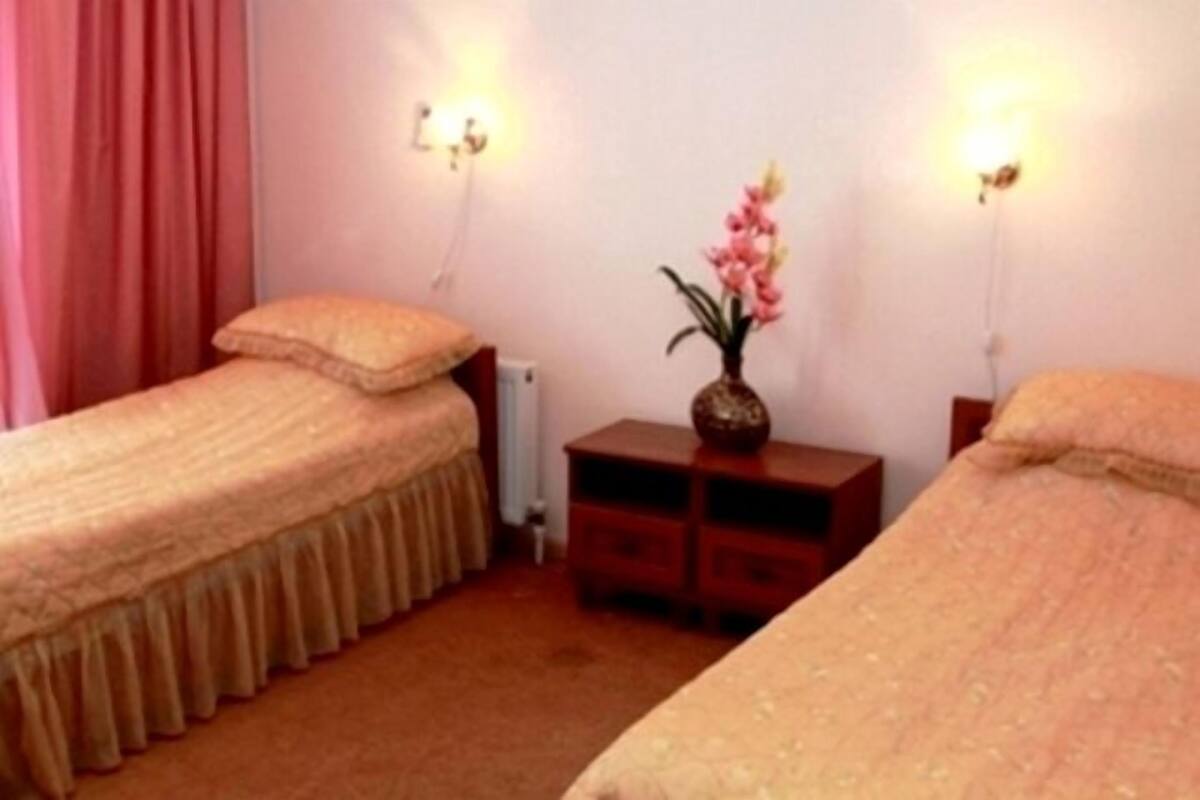 A room with two single beds, a nightstand with a vase of flowers, and wall-mounted lamps.