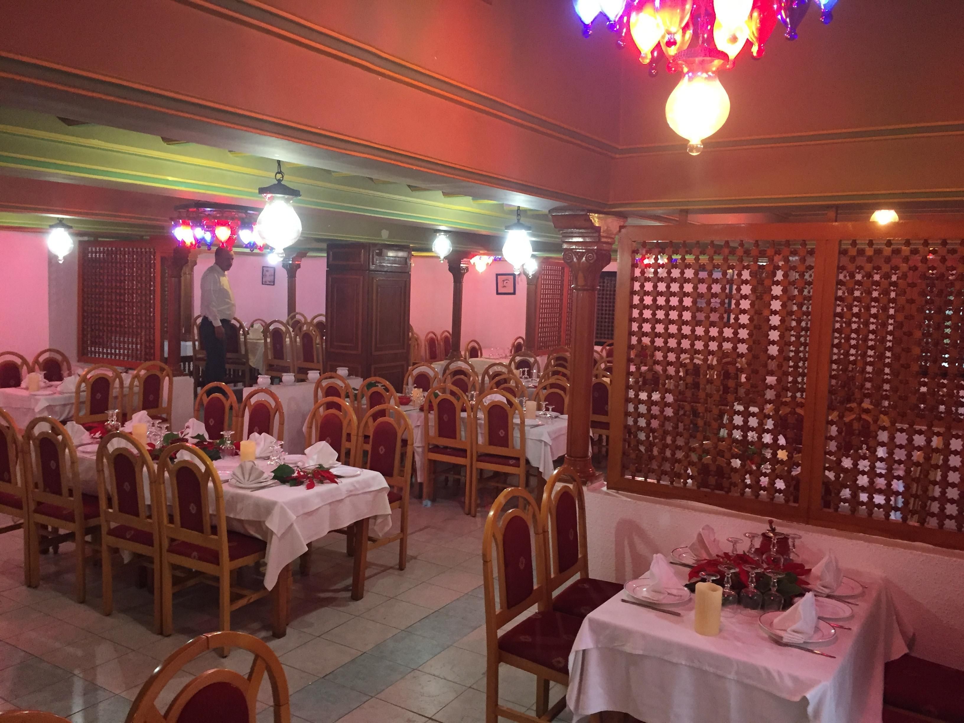 Un espace repas avec plusieurs tables dressées pour le service, des chaises en bois et un élément de séparation décoratif.