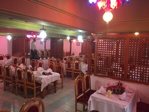 A dining area with multiple tables set for service, wooden chairs, and a decorative partition. - Residence Hammamet (Hammamet)