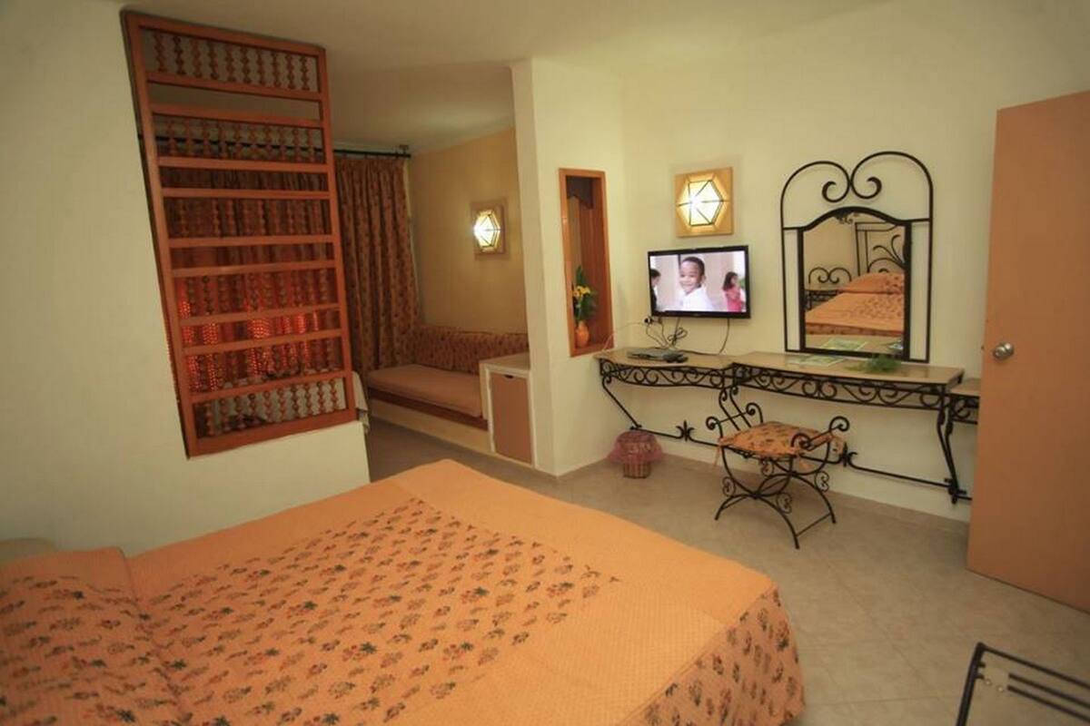 A bedroom with a bed, a desk with a computer, a chair, a television, and a decorative mirror.