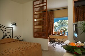 A bedroom with a bed, a TV, a small table with a vase of flowers, and a view of the outdoors. - Residence Hammamet (Hammamet)