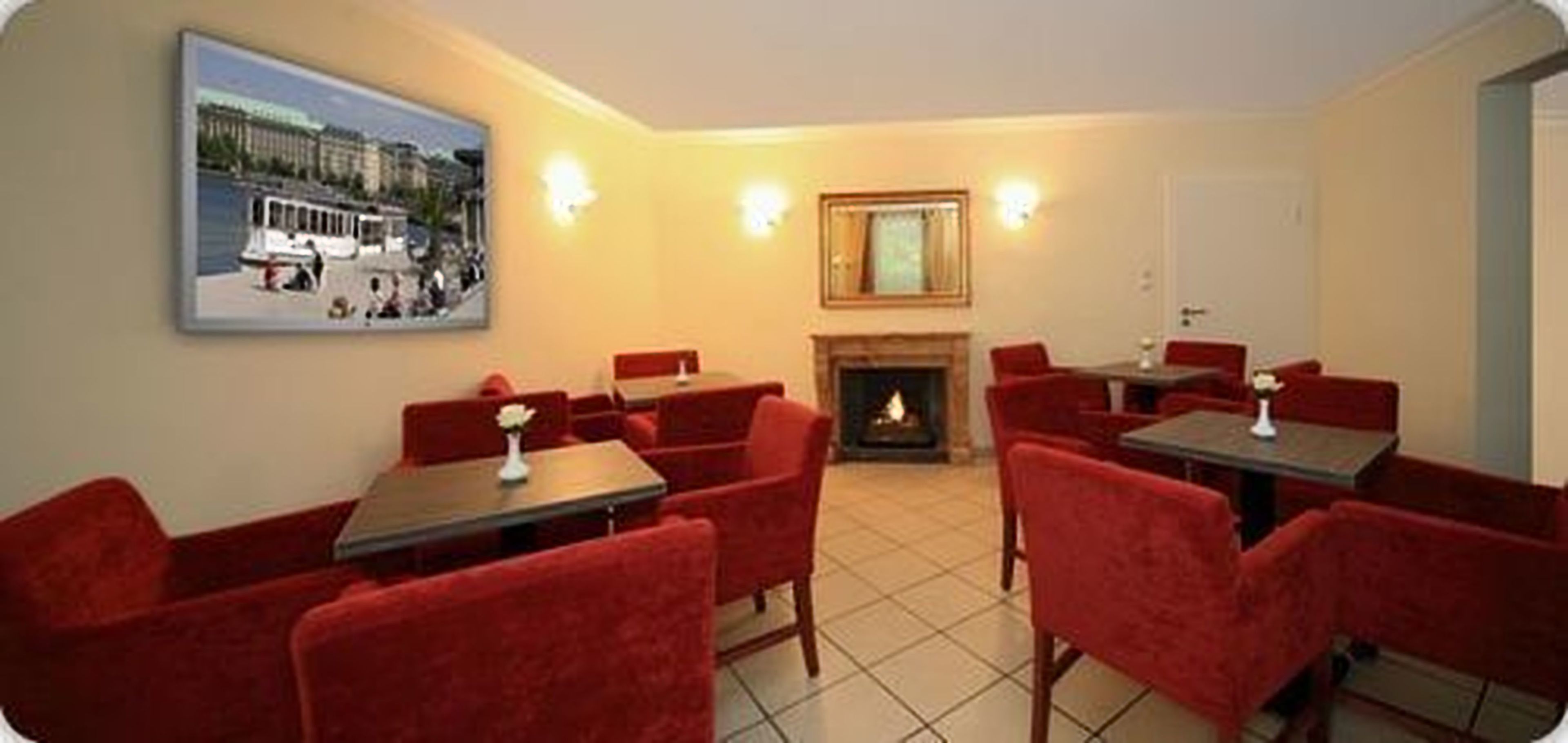 Habitación de hotel con sillones tapizados en rojo, chimenea y un ventanal con vistas a la ciudad.