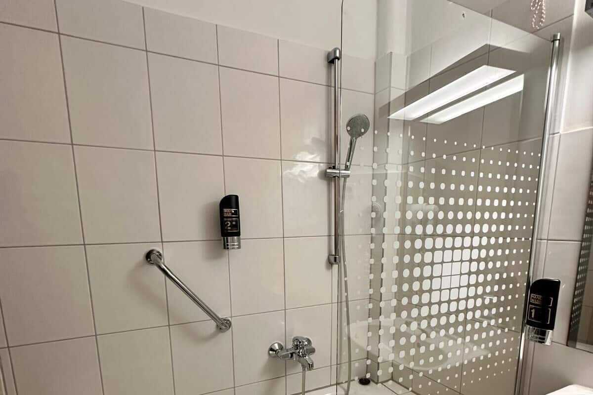 Un baño moderno con ducha envuelta en vidrio, cabezal de ducha manual y dispensador de jabón manual.