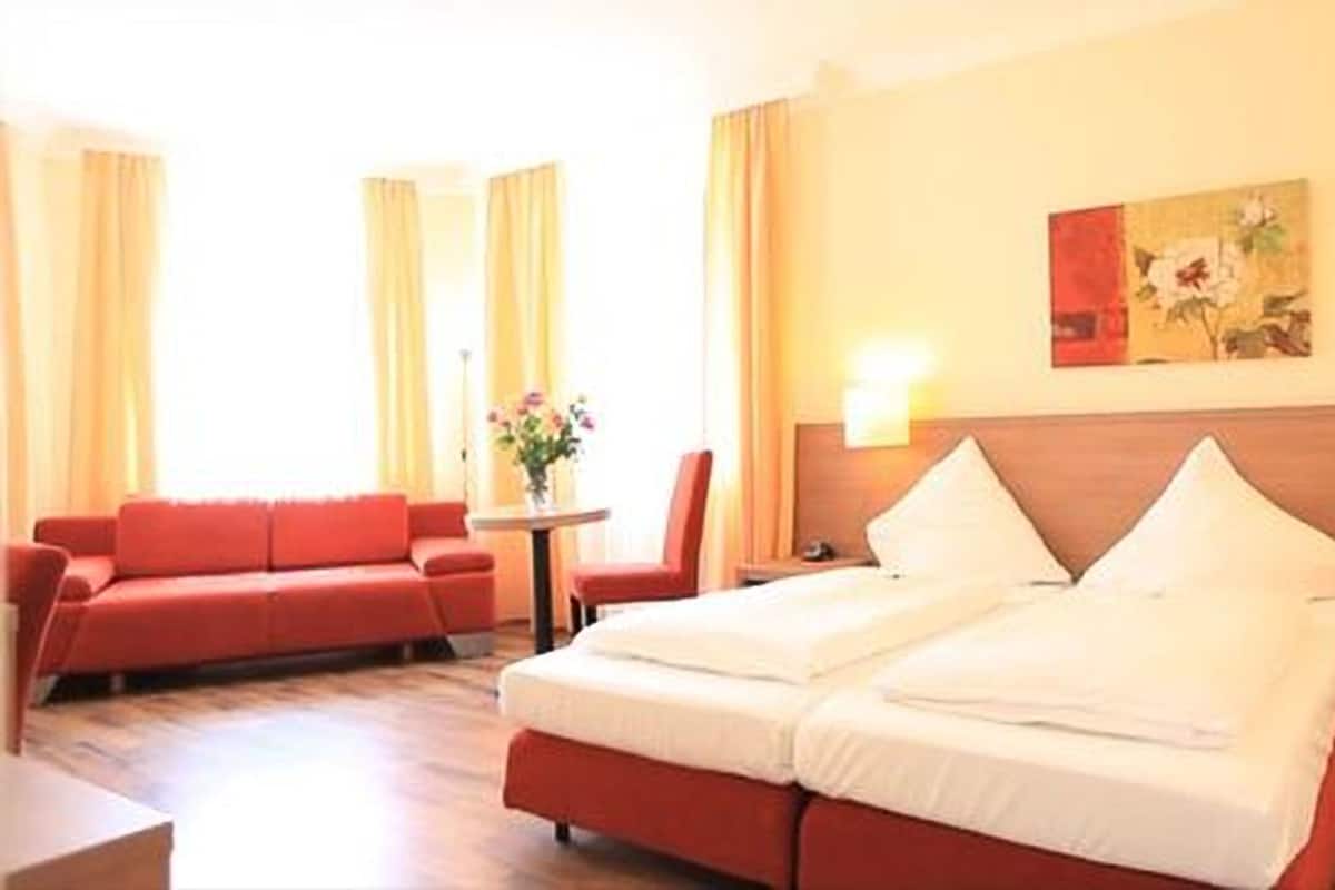 Una habitación de hotel con una cama doble, un sofá rojo, una mesita con flores y dos lámparas de noche.