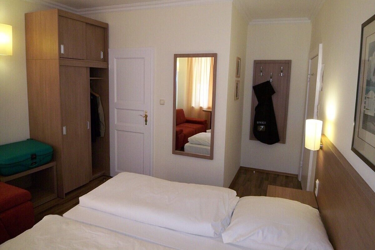 Habitación de hotel con cama, armario, espejo y una guitarra colgada en la pared.