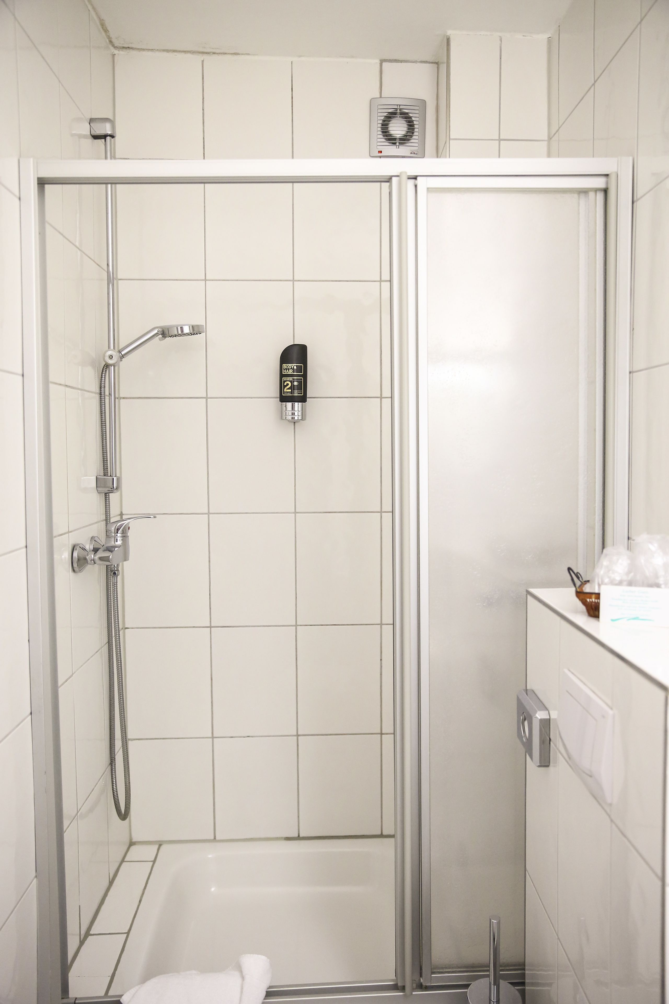 A modern shower enclosure with a control panel, a handheld showerhead, and a handheld faucet.