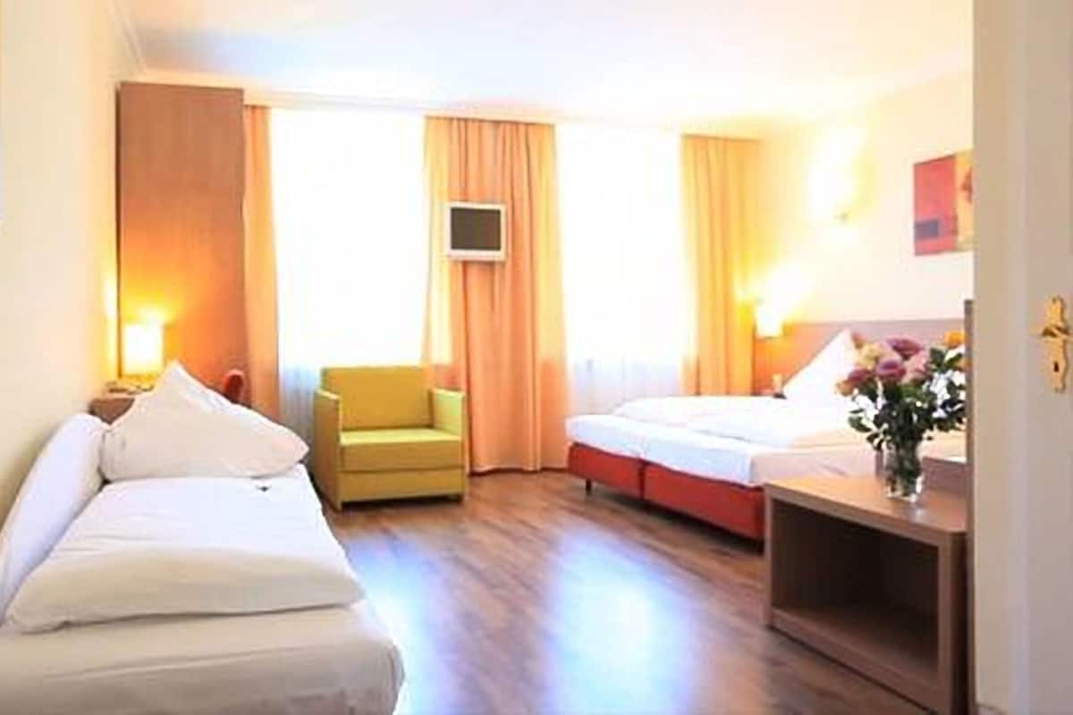 Una habitación de hotel con dos camas, una silla, un televisor y un escritorio con un jarrón de flores.