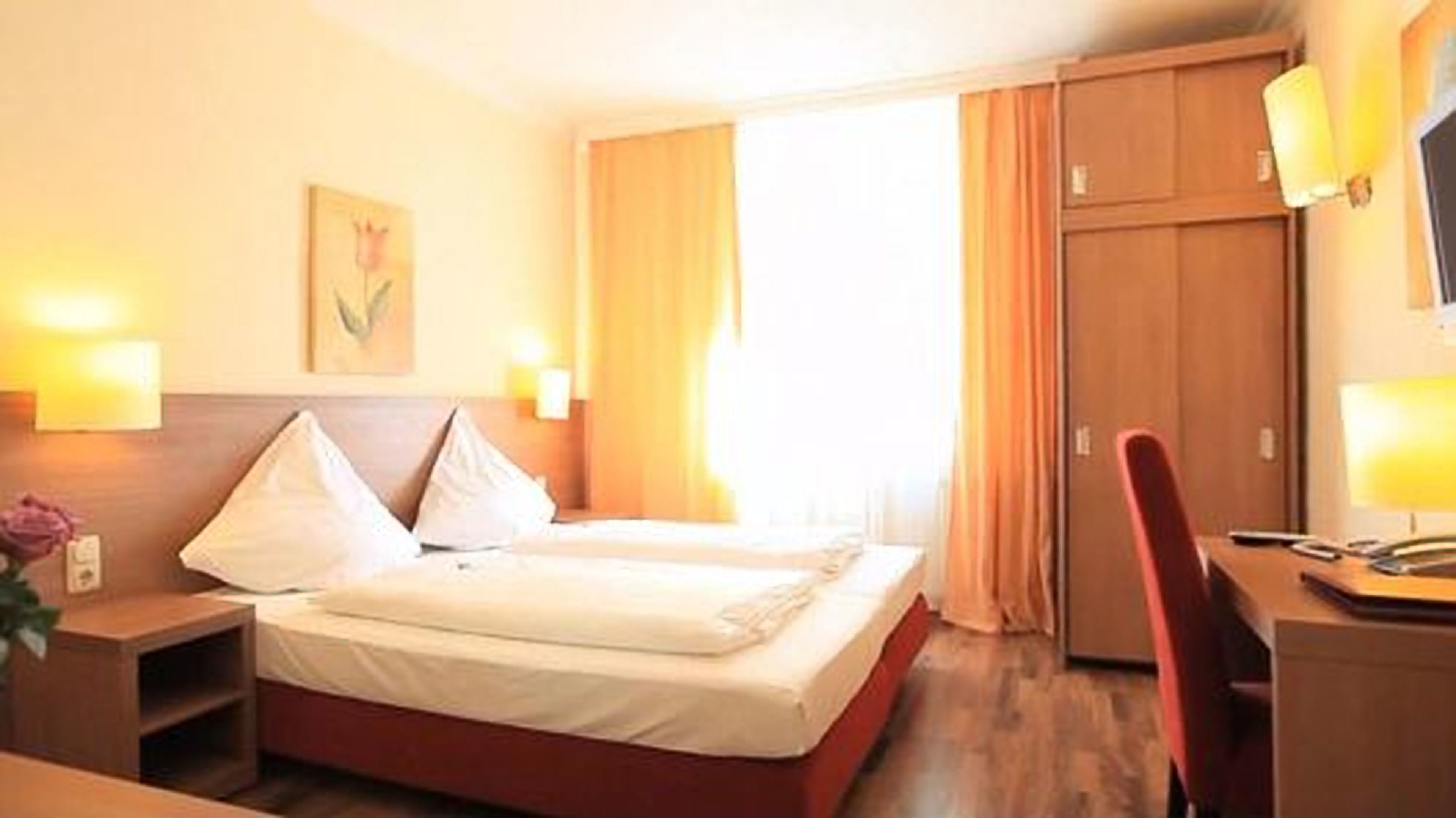 A hotel room with a bed, bedside tables, a desk, and a chair.