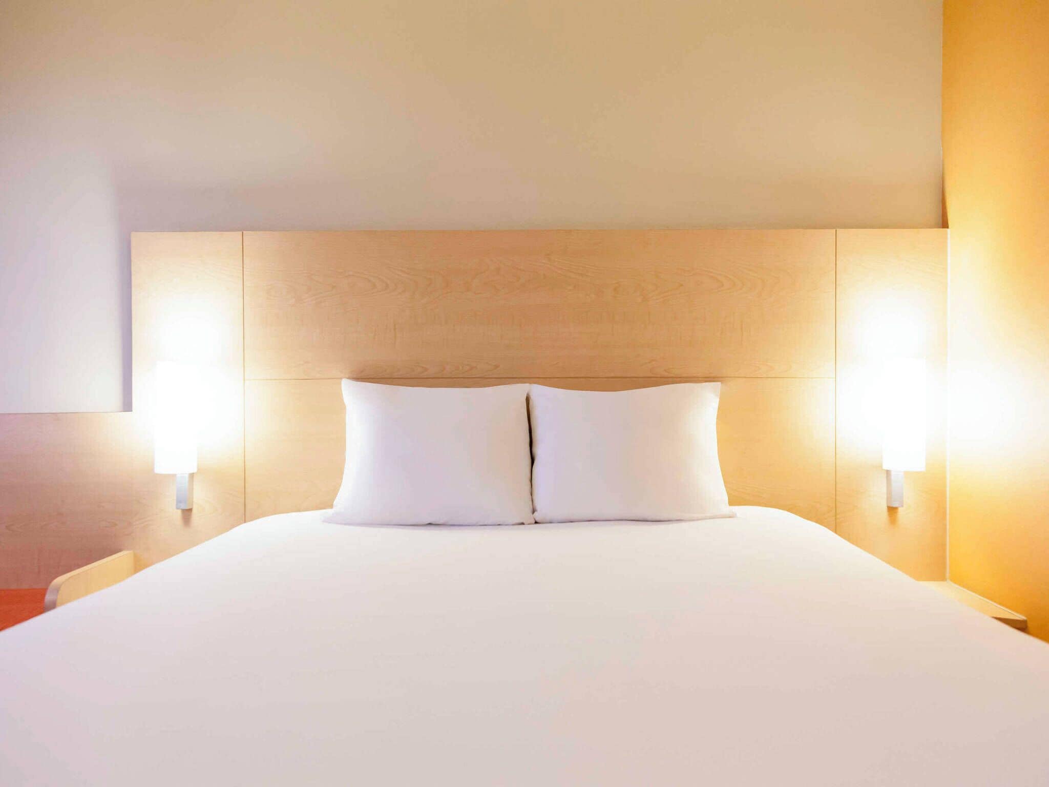 A neatly made bed with a wooden headboard and two wall-mounted light fixtures on either side.