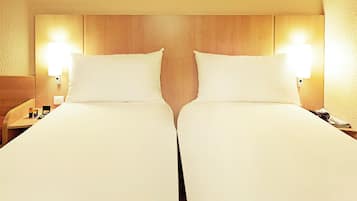 A hotel room with two beds, wooden headboard, bedside lamps, and a nightstand with a phone and a small table.