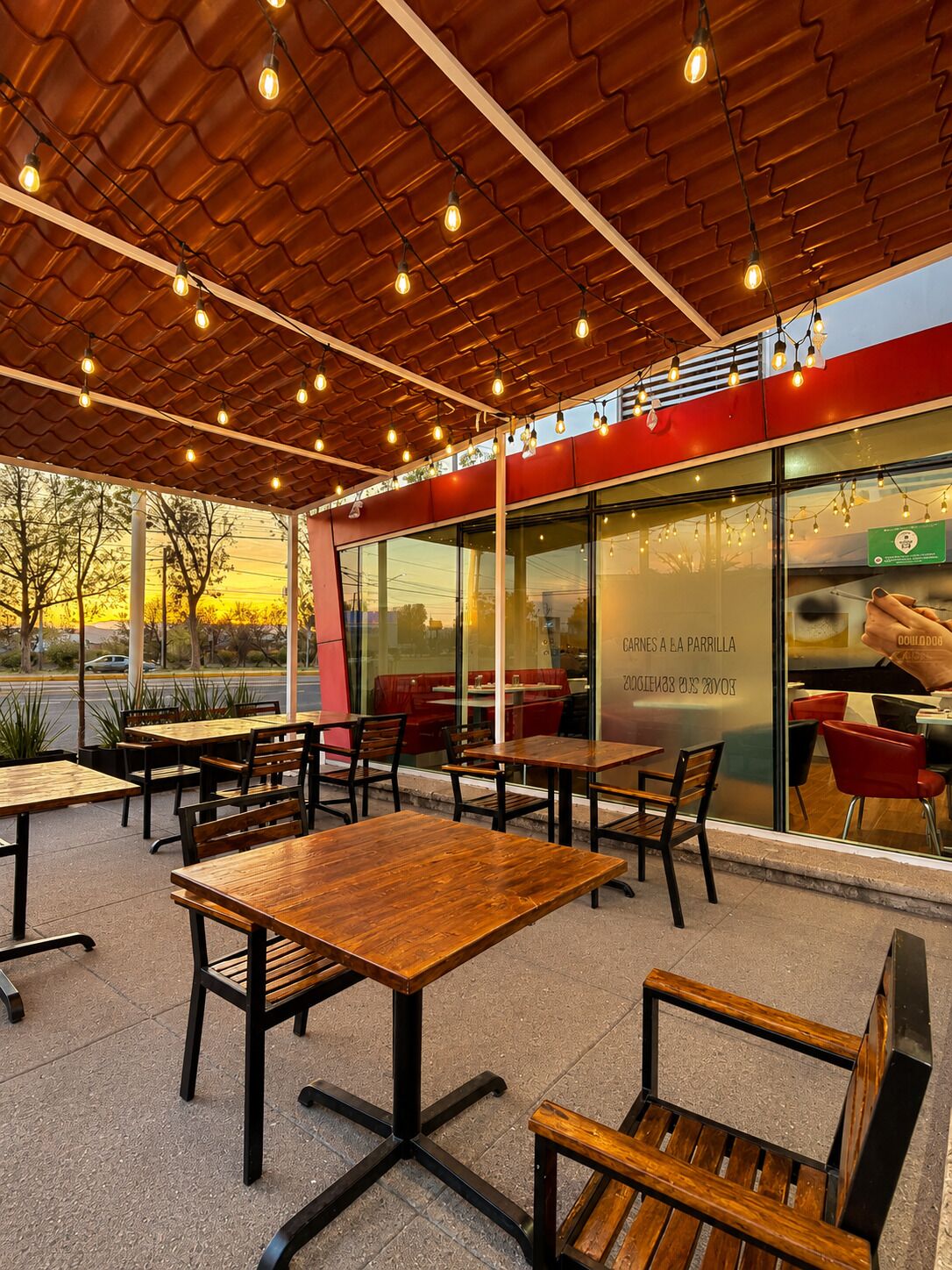 Un café en plein air avec des tables et des chaises en bois, une façade rouge et blanche et une vue sur la rue.