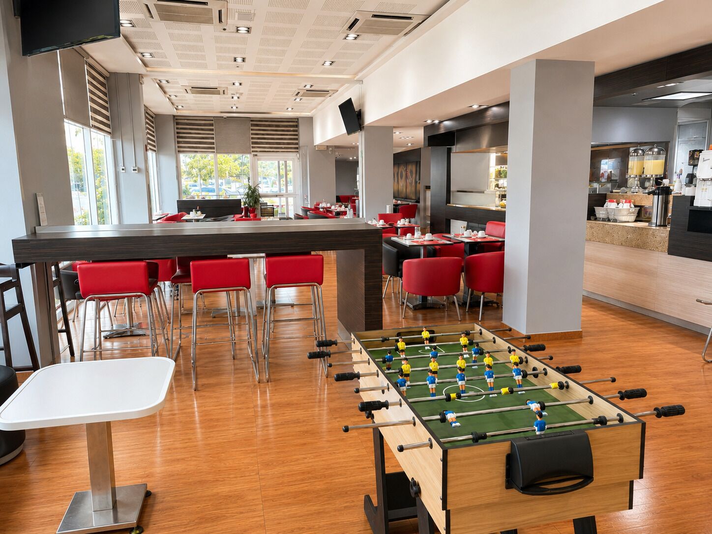 A modern indoor space with a foosball table, red chairs, and a bar area.