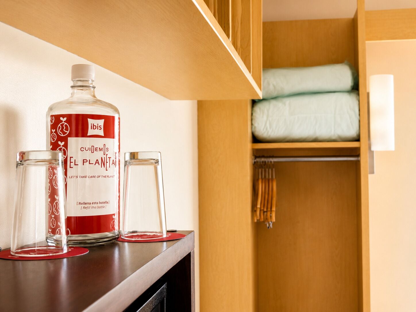 A bottle of Ibis El Plan Tail water, two glasses, and a neatly organized wooden closet with a folded blanket.