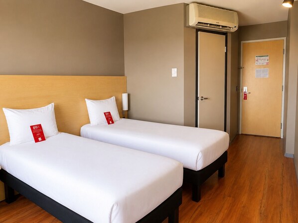 A hotel room with two beds, a wooden headboard, an air conditioning unit, a door with a fire alarm, and a wooden floor. - ibis Aguascalientes Norte (Aguascalientes)