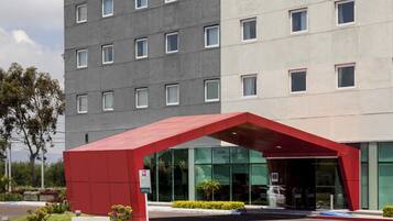 A modern building with a red entrance canopy, a parking area with blue parking spaces, and a multi-story structure with a grey facade.
